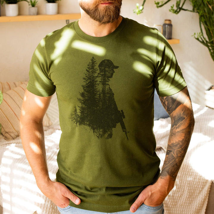 a bearded man wearing a green shirt with a picture of a man holding a gun