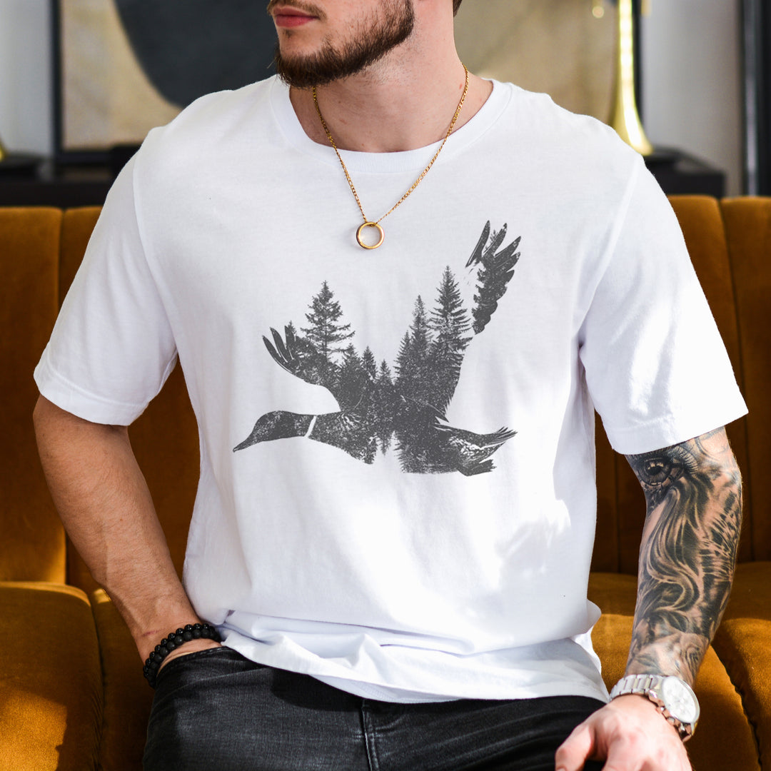 a man sitting on a couch wearing a white shirt with a bird on it